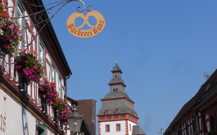 A sign shaped like a pretzel announces a bakery in one of Seligenstadt, Germany's many half-timbered houses. The tip of the Steinheimer Torturm, or gate tower, built in 1603, can be seen at center.