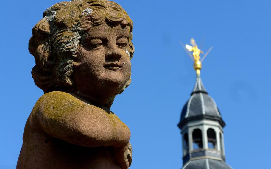 A cherub atop a wall in the cloister gardens of the former Benedictine abbey in Seligenstadt, Germany, with the tower of the Einhard Basilica in the background.