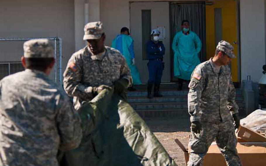 Morgue workers look on as soldiers from Logistics Task Force 35 work to construct a shower tent near the Ono Civic Center in Higashimatsushima, Japan. 