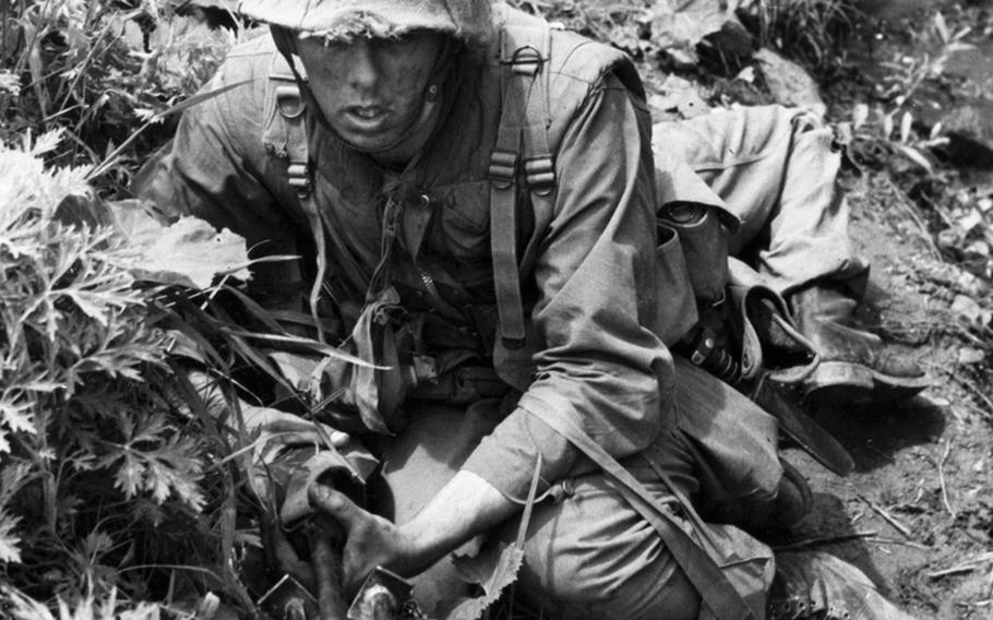 War-weary soldiers crouch in a ditch while enemy mortar shells drop nearby during a 1953 battle in Korea.