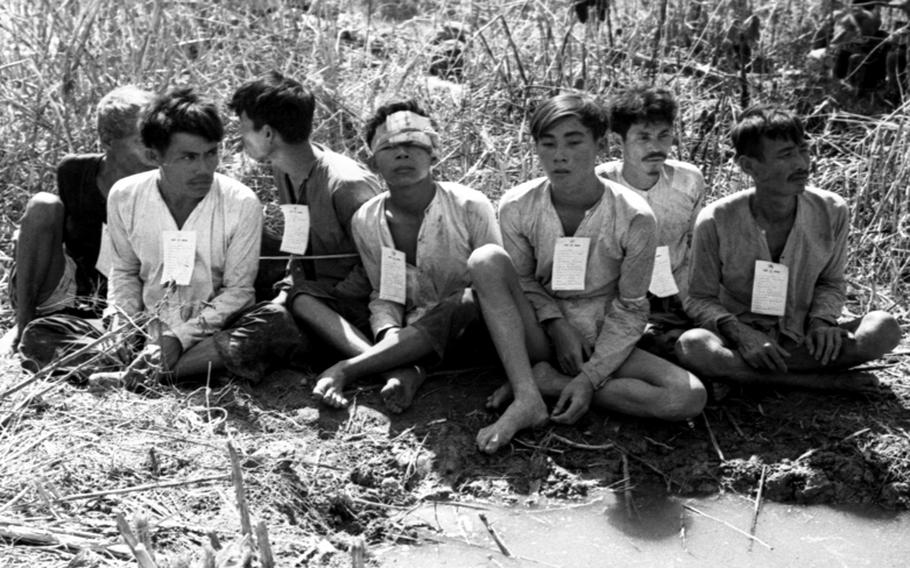 Viet Cong detainees, bound together, await transportation to an interrogation center.