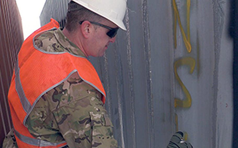 Chief Petty Officer Aaron Borg, with the U.S. Coast Guard Redeployment Assistance and Inspection Detachment team, spray paints the outside of a shipping container at Camp Marmal in Afghanistan with the letters NSW in February 2014. The letters stand for "not seaworthy," which means the container will not be shipped back to the United States.