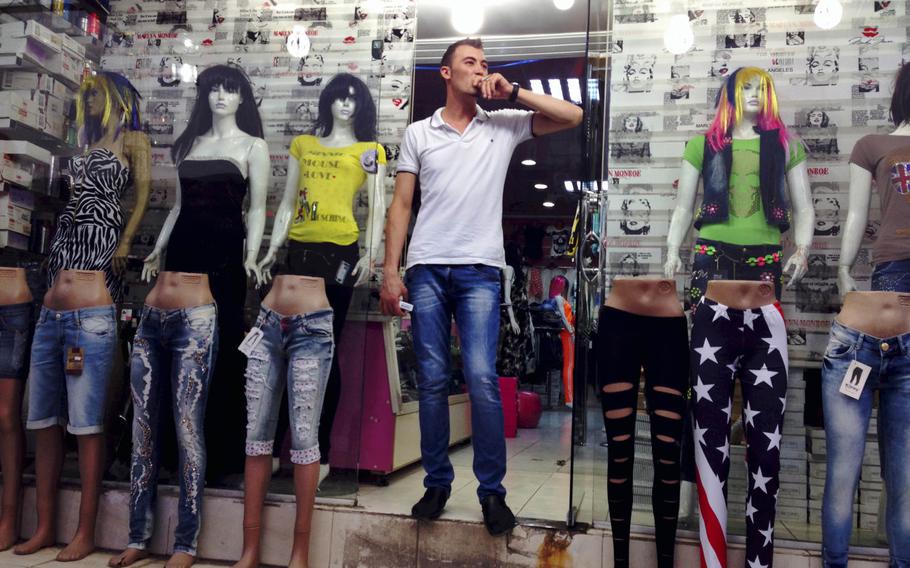 A retail worker in the Ankawa district of Irbil, capital of Iraqi Kurdistan, takes a smoke break next to mannequins sporting the ripped jeans and form-fitting T-shirts popular with Kurdish youngsters, Aug. 20, 2014.

