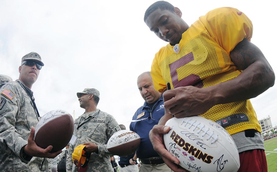 Fort Lee's Spc. Ruben Vazquez waits as Washington Redskins quarterback hopeful Pat White signs footballs during a special visit by soldiers to the team's training camp in Richmond, Va., Aug. 14, 2013.