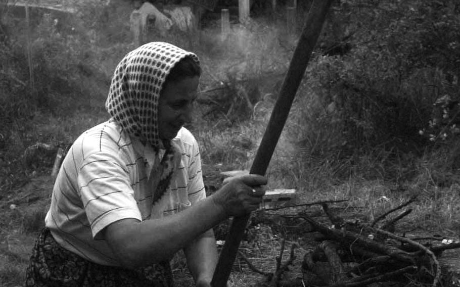 A Bosnian Muslim uses a makeshift hoe to clear what once was the front yard of her mountain village home in Jusici in September, 1996, while men in the background attempt to salvage what is left of a  war-ravaged house.