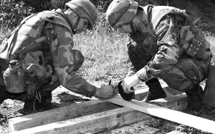 Sgt. Pierre Vandersteenen and Pfc. Paul St. Clair of B Co., 23rd Engineer Battalion, measure two-by-fours that they will cut for braces to be used to help secure the explosives that will be used to blow up the war-damaged railroad bridge over the Sava River east of Brcko in September, 1996.
