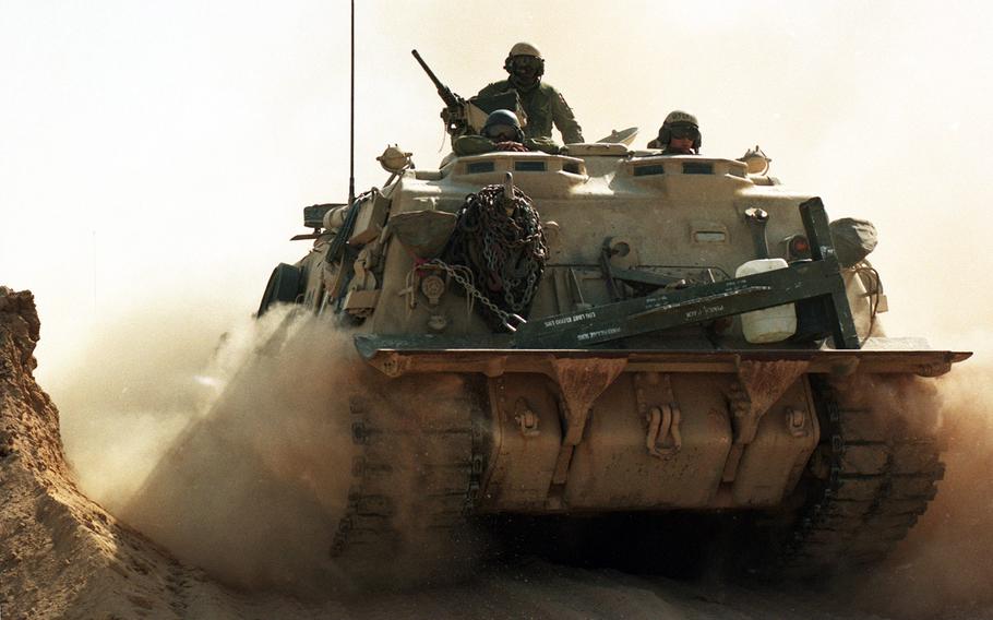 In February 1991, an armored vehicle passes through a breached sand berm separating Saudi Arabia from Iraq, paving the way for advancing allied troops during the Gulf War.