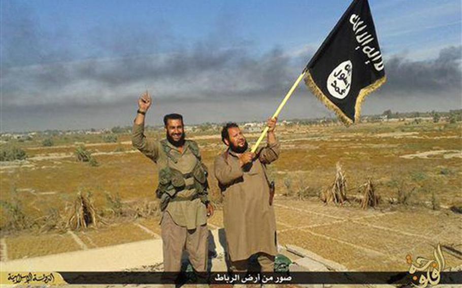 An Islamic State militant waves his group's flag as he and another celebrate in Fallujah, Iraq, west of Baghdad in a photo released on Sunday, June 28, 2015, on an Islamic State militant group website.