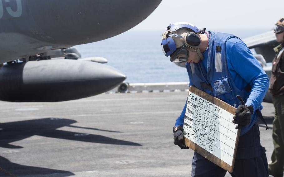 A member of the flight deck crew on the amphibious assault ship USS Boxer holds up a board to communicate with the 13th Marine Expeditionary AV-8B Harrier pilots preparing to launch in support of Operation Inherent Resolve on Thursday, June 16, 2016.  