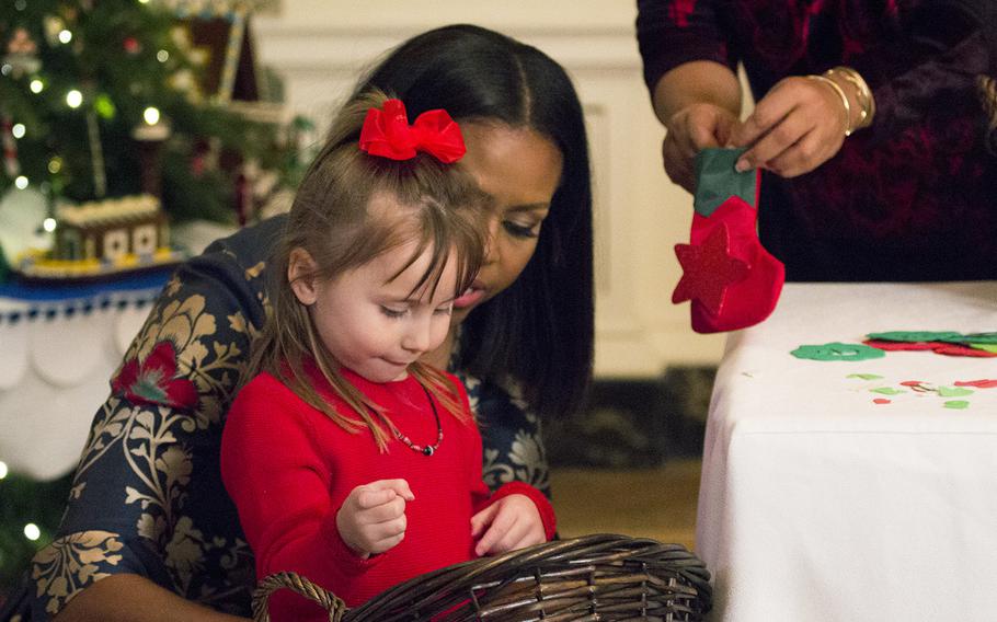 First Lady Michelle Obama helps a girl decorate a stocking at the White House on Nov. 29, 2016. Obama invited military families to the White House to preview holiday decorations.