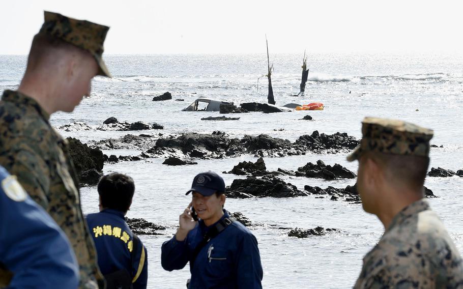 Officers of Okinawa Prefectural Police and U.S. military investigate the site where debris of a U.S. military MV-22 Osprey, background, was spotted in shallow waters off Nago, Okinawa, southern Japan, Wednesday, Dec. 14, 2016, after its crash-landing.