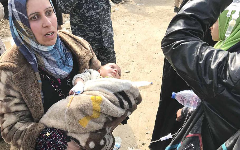 On the outskirts of Mosul, a woman holds her ill infant, who was receiving intravenous fluids, while waiting for transportation to a displacement camp south of the city on Wednesday, March 8, 2017.