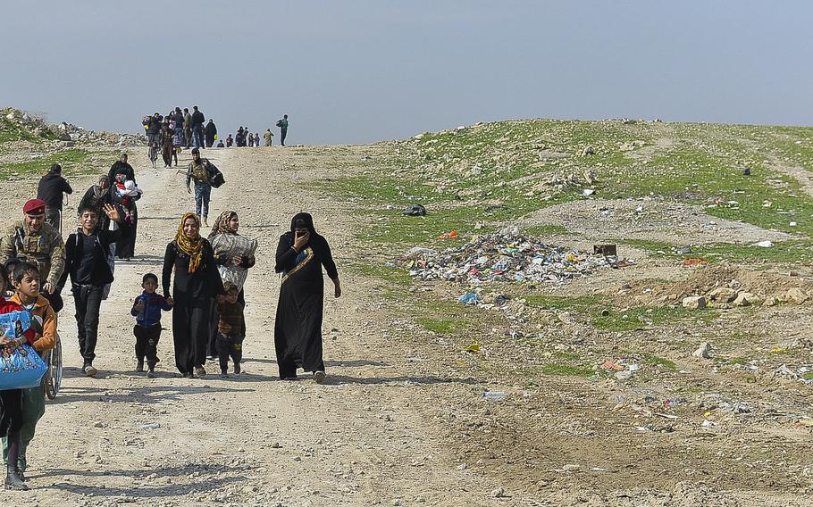 Families fleeing violence in Mosul, Iraq stream over a hill near the city's airport, where Iraqi military and police officials were waiting to pack them onto buses and trucks to be taken to a displacement camp south of the city on Wednesday, March 8, 2017.
