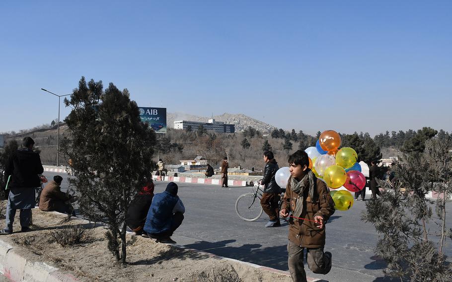 A boy carried balloons across a road in front of the Intercontinental Hotel in Kabul, Afghanistan, on Sunday, Jan. 21, 2018, as security forces worked to clear the building of Taliban attackers. Blasts and gunfire could be heard Sunday morning, more than 15 hours into the attack.