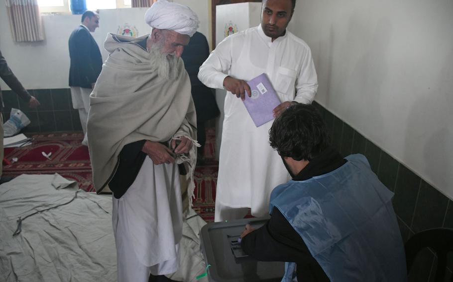 An election official helps a man cast his ballot for Afghanistan's parliamentary elections on Sunday, Oct. 21, 2018. Voting at the polling station was extended for a second day because of various complications.