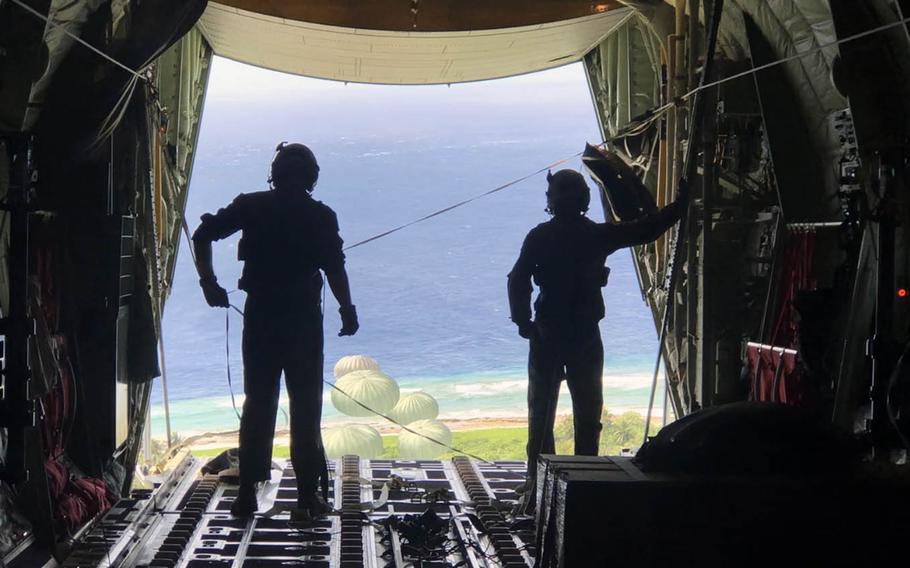 Staff Sgt. Chris Hofer and Senior Airman Walter Frank watch as parachutes open to carry Operation Christmas Drop donations to islanders below. 
