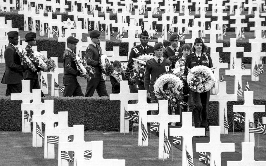 Representatives of various military services walk through the Cambridge American Military Cemetery with wreaths to honor the 3,812 fallen and 5,125 names on the Wall of the Missing in June, 1994.