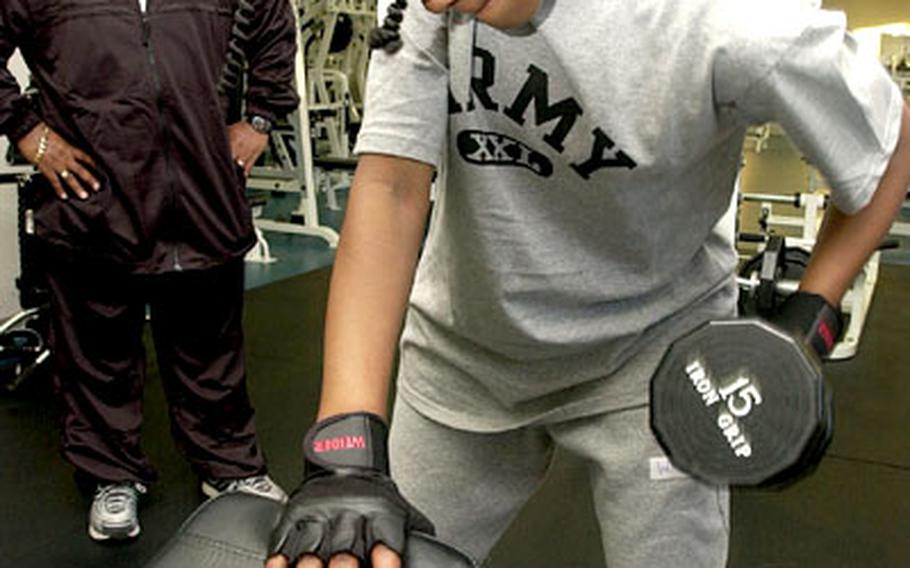 Brittanie Williams, a participant in the Youth For Power program, performs a dumbbell row exercise while Vincent Allen watches her form at the Yano Fitness Center at Camp Zama.