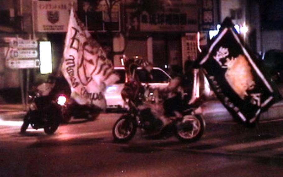 Okinawa&#39;s Bosozoku often defy traffic laws, making illegal u-turns on busy city streets to parade their colors. These flags announce that the Ishikawa "Noise Kids" are in town. The photo is from a police videotape.