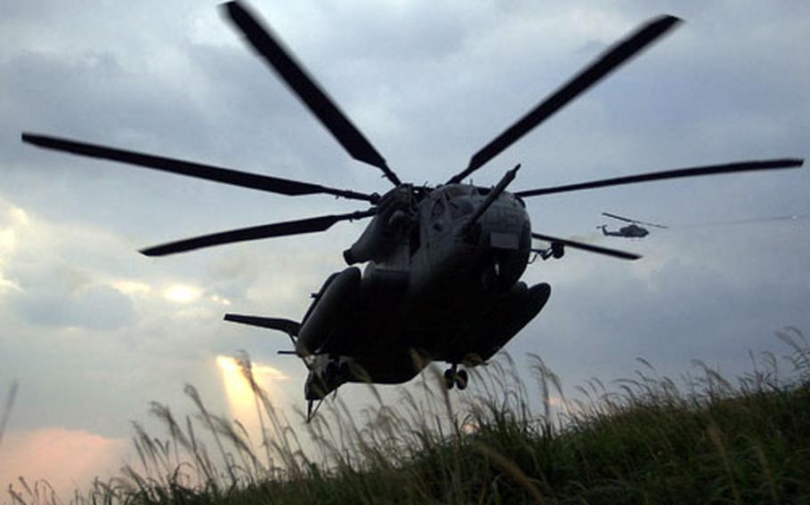 A Marine CH-53E Super Stallion flares out for a landing while a AH-1W SuperCobra in the background fires rockets to suppress targets during insert and extract drills off Okinawa.