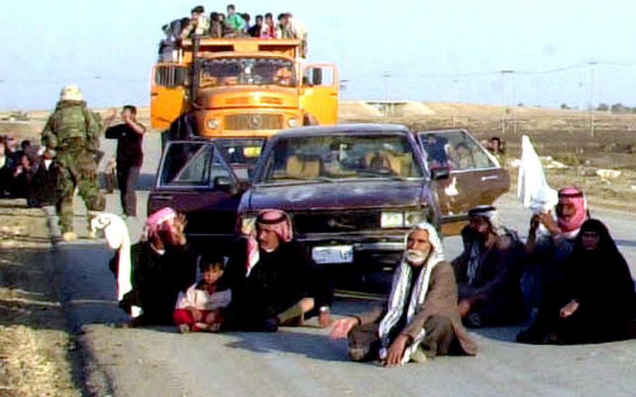 Travelers in Iraq wait as civilian vehicles are inspected by U.S. troops.