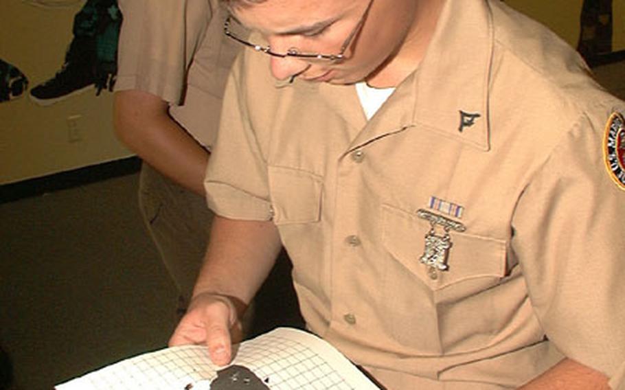 Matthew Willis, a cadet lance corporal in Kubasaki High&#39;s JROTC, counts his shot holes to see how he scored during air pistol qualification on Okinawa.