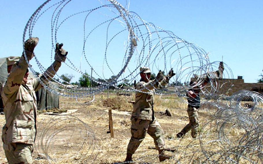 Master Sgt. Daniel Wear, Staff Sgt. Chip Davidson, and Staff Sgt. Brian Curtis, left to right, hoist a strand of concertina wire to help secure a living area.