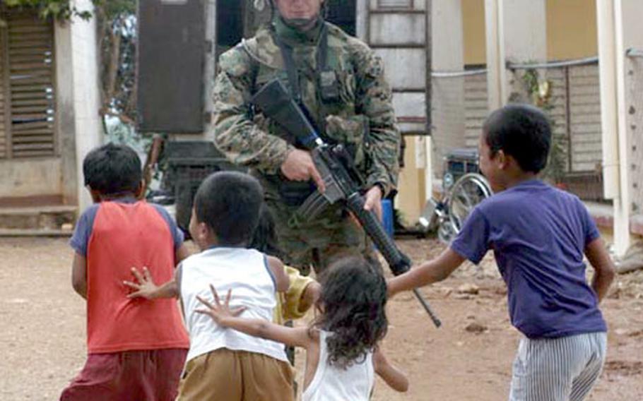 Armed Marines watch children play during a Medical Civil Action Project, or MEDCAP, held by U.S. and Philippine forces near Zamboanga City in the Southern Philippines. Military and civilian medical personnel treat villagers while a contingent of Marines patrols the surrounding village and guards the grounds of the MEDCAP. Travel to the location requires a multi-vehicle convoy including armored humvees. Occupants wear Kevlar body armor and each vehicle must have several weapons inside.
