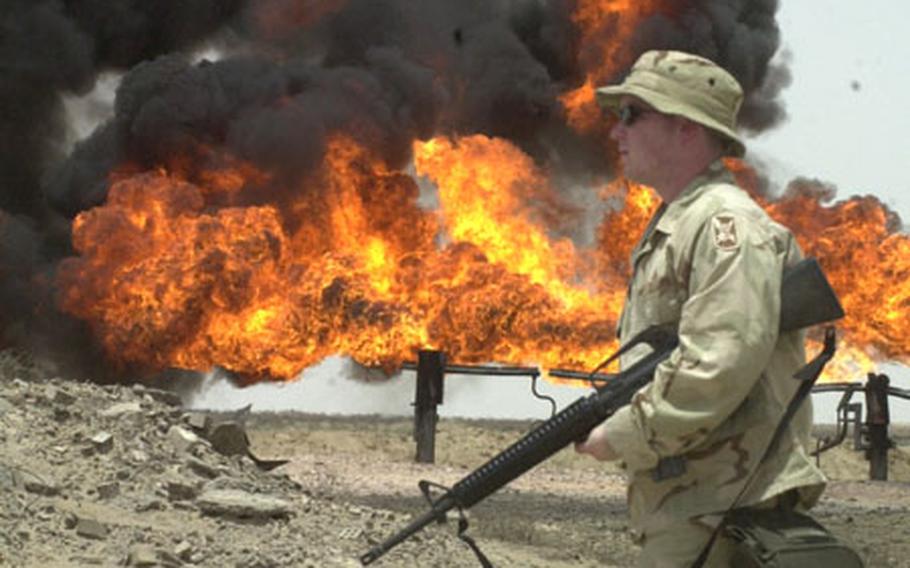 Spc. Joseph Feagin, 25, of Charleston, S.C., strolls past burning gas fires at an oil processing plant near Rumallah, Iraq.