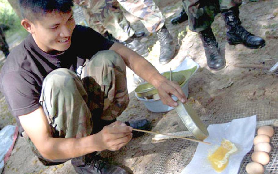 Royal Thai Marines demonstrate cooking an omelette on an oiled sheet of paper over fire during a jungle survival class for U.S. Marines during Cobra Gold in Thailand.