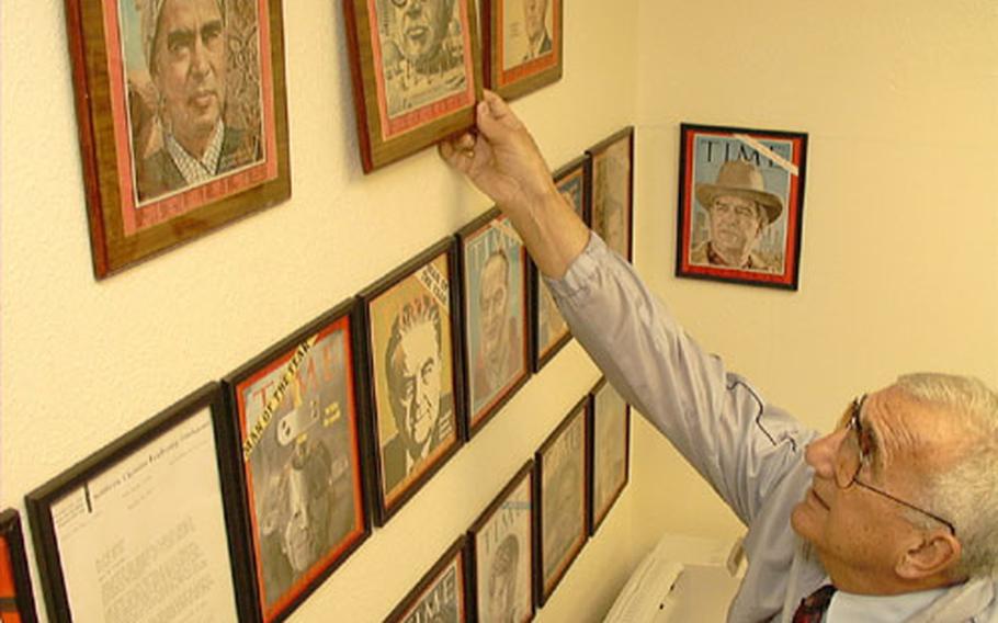 At Kadena Air Base, educator Greg Apkarian reaches for a picture frame that has a personalized autograph of architect Buckminster Fuller, featured on a 1964 Time magazine front cover.