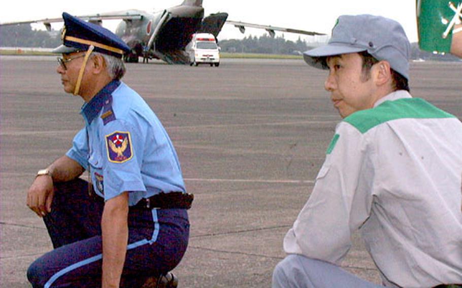 Tokyo government officials watch the runway while an ambulance unloads from the back of a Japanese C-1 aircraft.