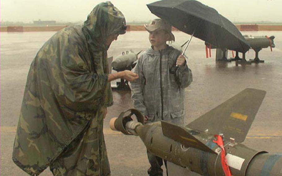 On the rainswept flight line at Osan Air Base, South Korea, Maj. Chuck West covers a few fine points about bombs with his son Andrew, 9, a fourth-grader at Osan American Elementary School. West is with the 303rd Intelligence Squadron. Although rain forced cancelling the base&#39;s second annual Air and Space Power Day, father and son braved a drenching for a look at the aircraft and ordnance that had been set up for display.