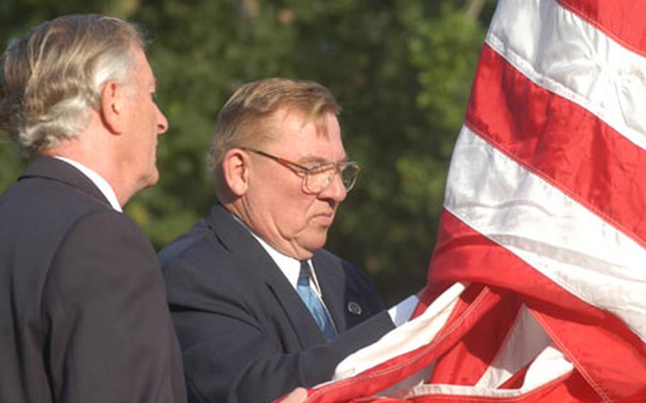 Bob Stone, left of the Royal British Legion, and Jim Schoenecker, superintendent of the Cambridge American Cemetery, raise a flag early Thursday at the cemetery. The flag belongs to an American veteran&#39;s widow and once flew above the White House. The ceremony also marked events of Sept. 11, 2001.