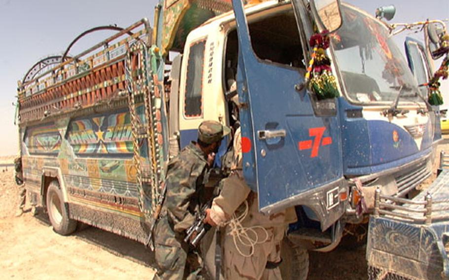 Sgt. Jason Garrison, 10th Military Police Company, and a soldier from the Afghan militia forces inspect the cab of a "jingle truck" at a checkpoint in Kandahar Friday. The trucks have ornate chains dangling from the frame that jingle when they drive, thus the name. Nothing suspicious was found on the truck.