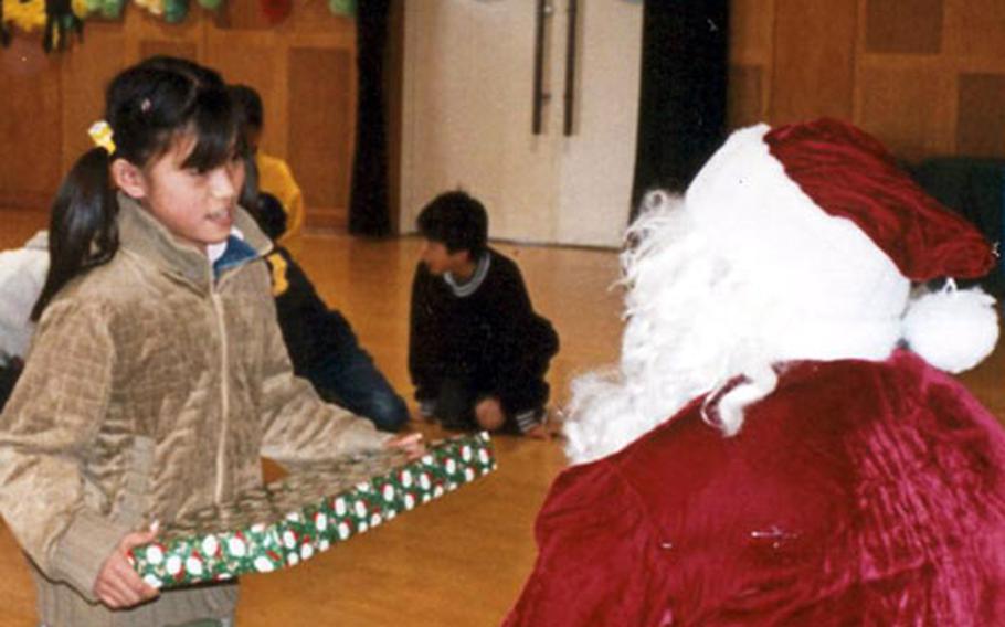 Dressed as Santa Claus, Cpl. Shane Bailey from the Marine Aviation Group 12 headquarters, and the coordinator of Toys for Tots in 2002, hands a young Japanese girl a Christmas present last year at a local orphanage.