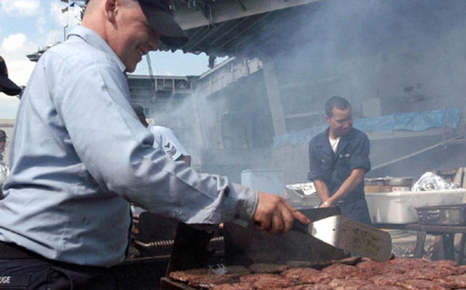 Seaman Dachmon Ruge, a mess specialist aboard the USS Kitty Hawk, grills burgers in front of the carrier to celebrate the ship&#39;s return from drydock Friday at Yokosuka Naval Base, Japan.