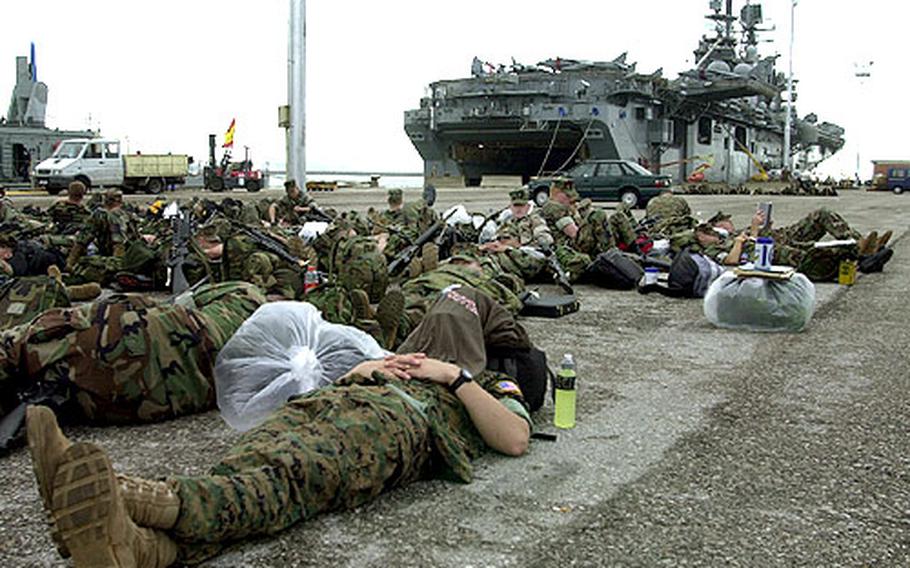 A group of Marines rests pierside on Tuesday with the USS Iwo Jima in the background at Naval Station Rota, Spain.