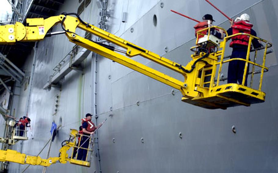 Sailors on cranes paint the side of the USS Iwo Jima on Tuesday at Rota.