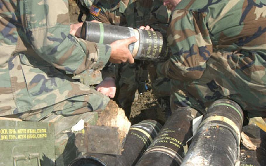 From left, Sgt. Eric Grieve, Staff Sgt. Kevin Howard and Sgt. Paul Bartells, all of Company B, 2nd Battalion, 236th Infantry Regiment, struggle to take a 122 mm armor-piercing artillery round from its storage tube. They were helping the 666th Explosive Ordinance Detachment prepare ordnance for destruction.