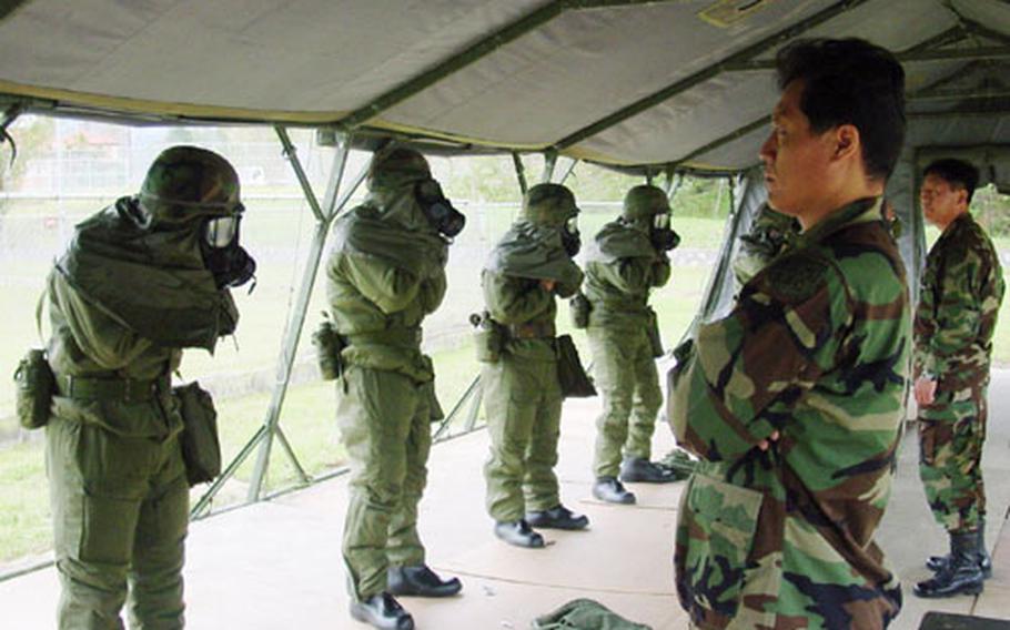 Evaluators watch as members of the 37th KSC Company put on their M40 protective masks during a training test at Camp Carroll.