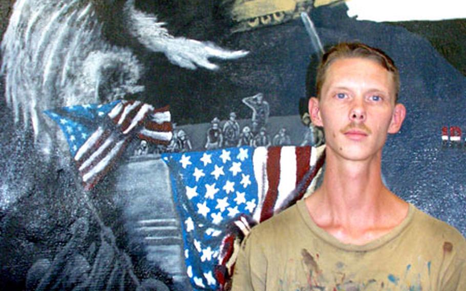 Army Staff Sgt. Timothy Himburg stands in front of a mural he painted at Camp Dogwood. Many of Himburg’s murals are scattered throughout the camp. “It helps me pass the time,” he said.