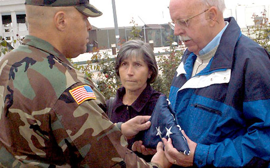 Lt. Col. Kevin Gutknecht, left, of Task Force Iron, commander of Camp McGovern, presents the U.S. flag to Charles McGovern, the brother of 1st Lt. Robert McGovern, the soldier for whom the camp was named, in a small ceremony on Sunday. In the middle is Charles’ wife, Wally McGovern.