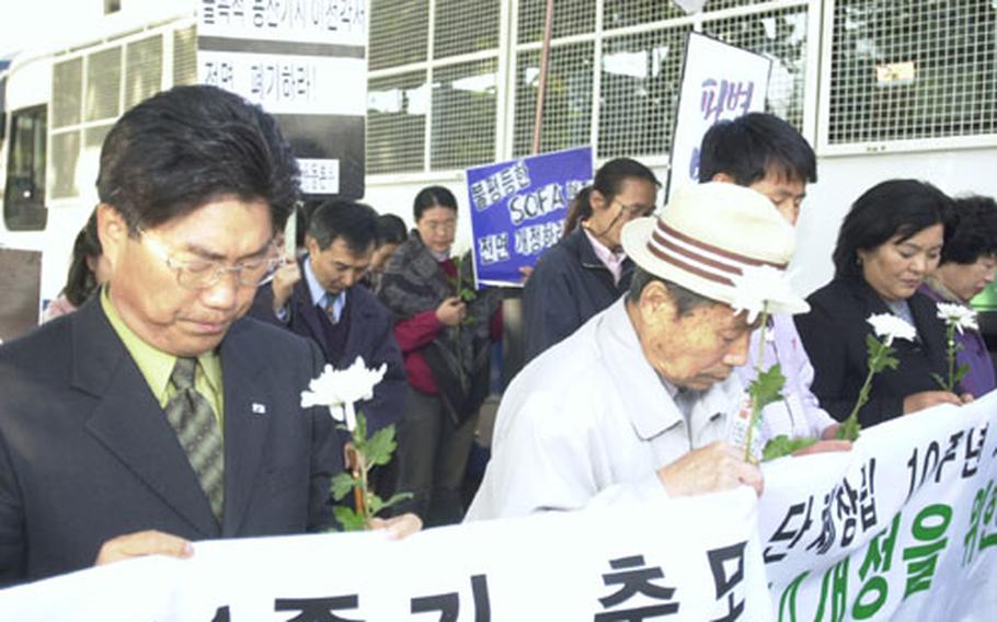 Holding memorial flowers for alleged victims of crimes by GIs, members of a protest group pause for a moment of silence during the final gathering by the group, which has spent ten years focusing on the issue.