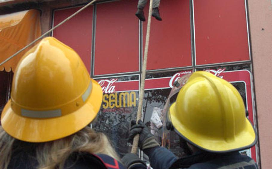 Firefighters from different towns pull ropes apart to allow for the safe landing of a boy being lowered from a window in a drill demonstrating civilian evacuation from a building on fire.