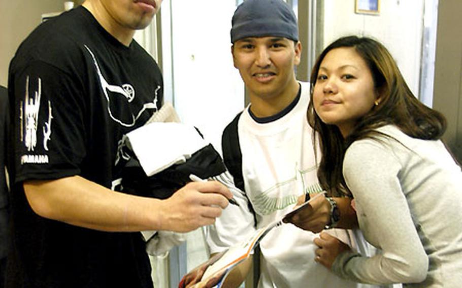 Staff Sgt. Tony Eclavea, from Kadena’s 18th Equipment Maintenance Squadron, and girlfriend Noriko Tonoshiro pose with and get an autograph from K-1 fighter Musashi at the Okinawa Convention center.