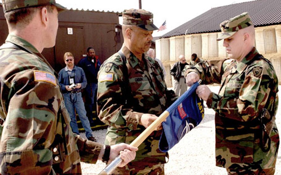 Maj. Robert Leasure, right, removes the Area Support Team McGovern flag from the mast extended by Master Sgt. Larry Fisher, left, at a flag deactivation ceremony Tuesday at the camp. Col. Joe Croom, commander of Area Support Group Eagle, received the flag. The camp is slated for closure later in the year.