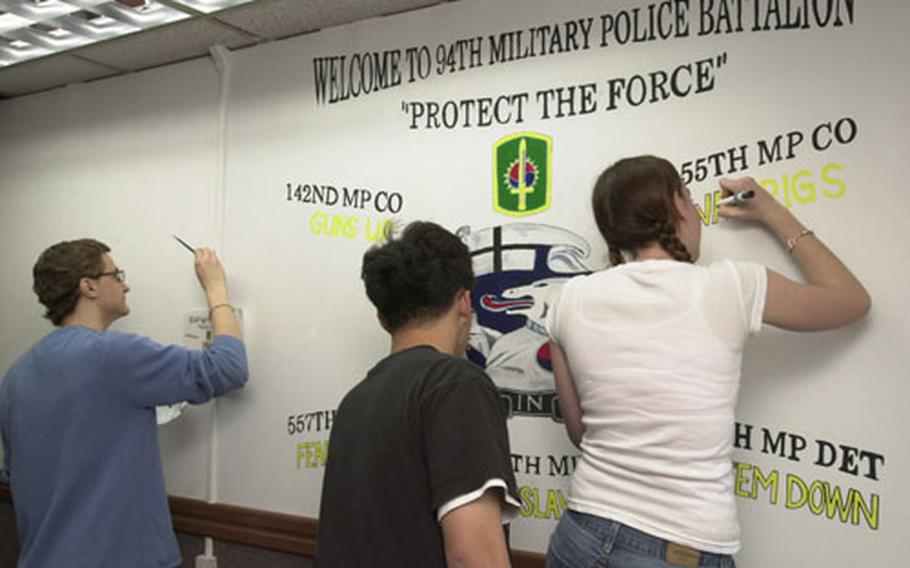 Seoul American High School Students (l to r) Peter Orrahood, Jonathan Yi, and Sara Wilson put the finishing touches on a mural they helped create for the 94th Military Police Battalion at Yongsan Garrison.