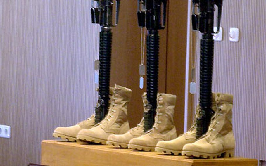 Boots, rifles and helmets are displayed on a podium in front of photographs of the three fallen soldiers.