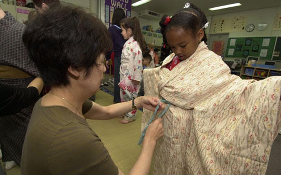 Kindergartener, Dominique Goden gets prepped for her obi to be tied on her kimono from Hiroko Kuga during the Nihon Matsuri festival held at Yokota West Elementary School Wednesday.